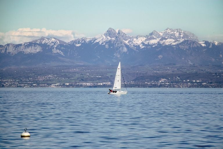 A sailboat glides on Lake Geneva with the majestic Alps in the background, capturing serene nature.